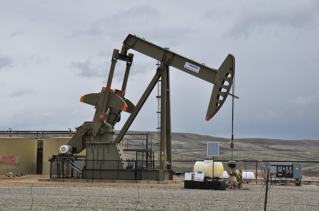 Oil pump jack and equipment at remote industrial site under cloudy sky.