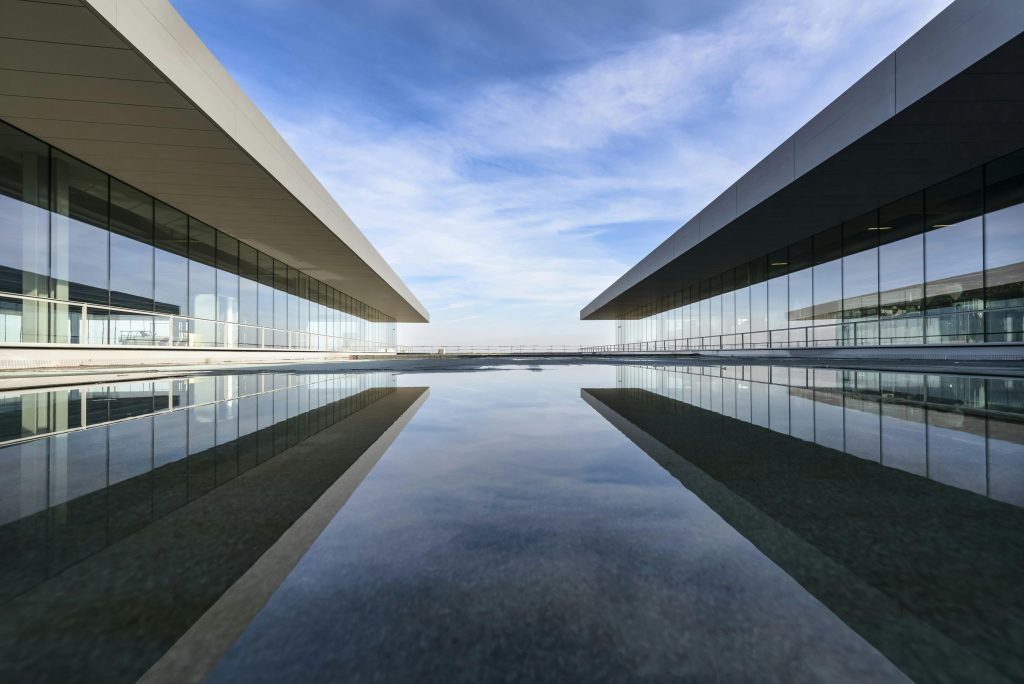 Futuristic glass building mirrored on a still water surface with a cloudy sky.